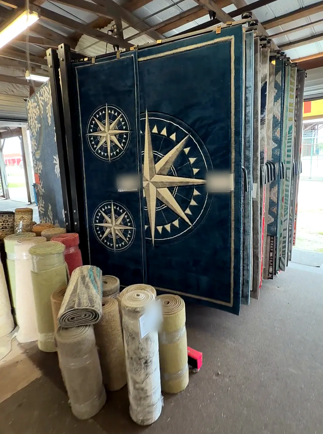 Navy compass-rose rugs on a swing rack with rolled runners standing in front; tags blurred.