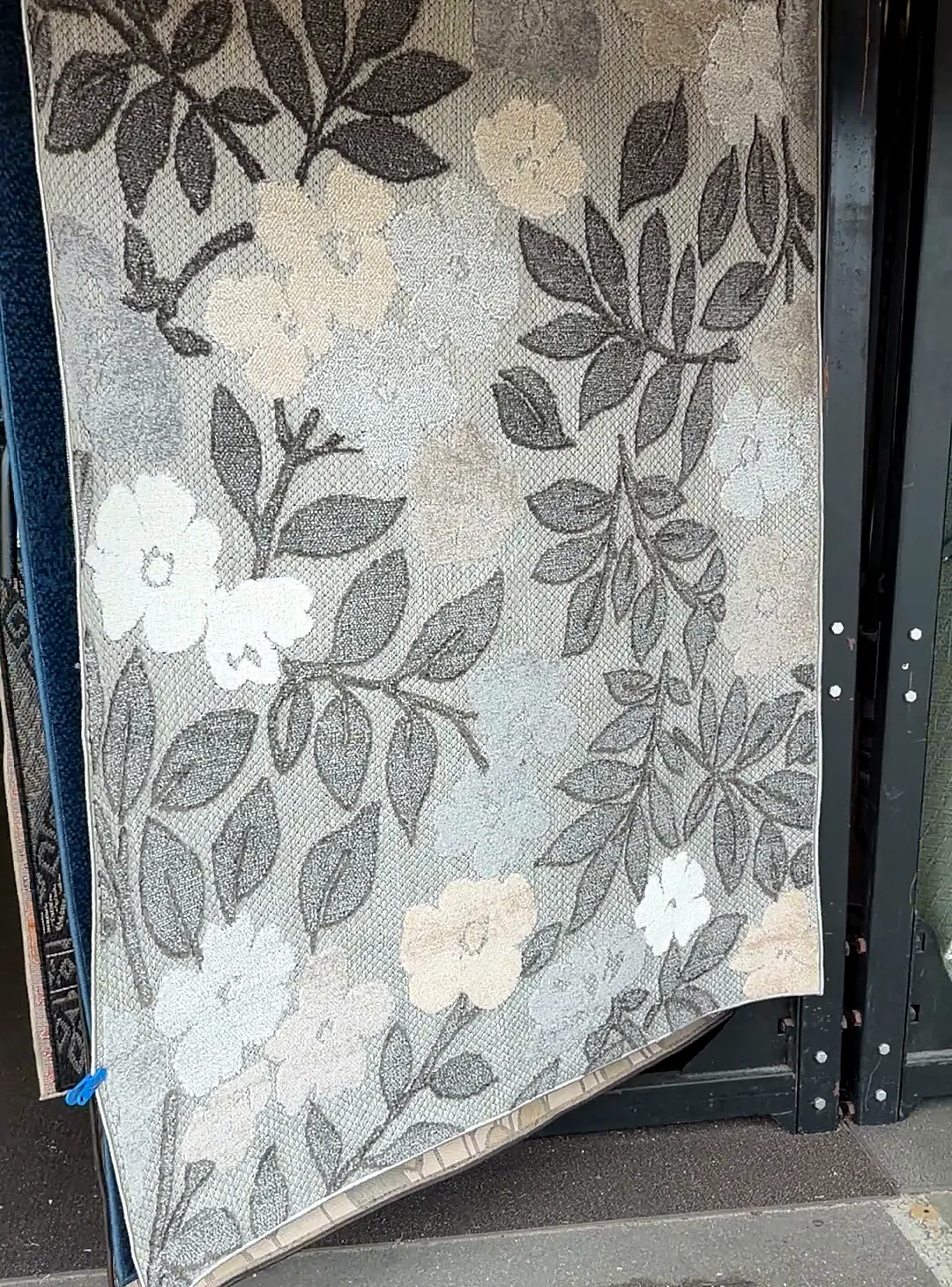A gray leaf-pattern rug hanging on a rack just inside the doorway, beside a wooden post.