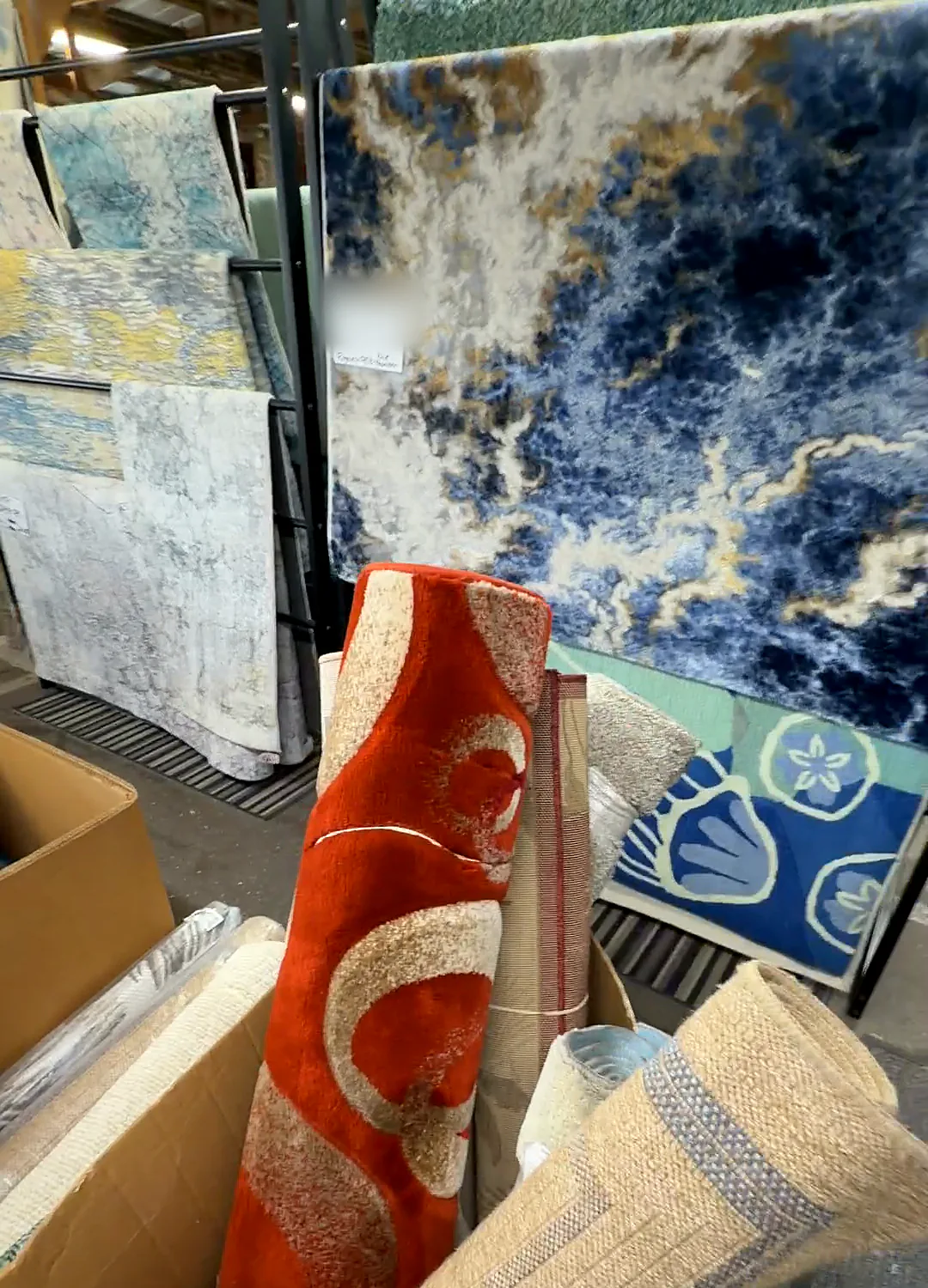A midnight blue and gold marbled rug hanging behind a rolled red rug with a white swirl.