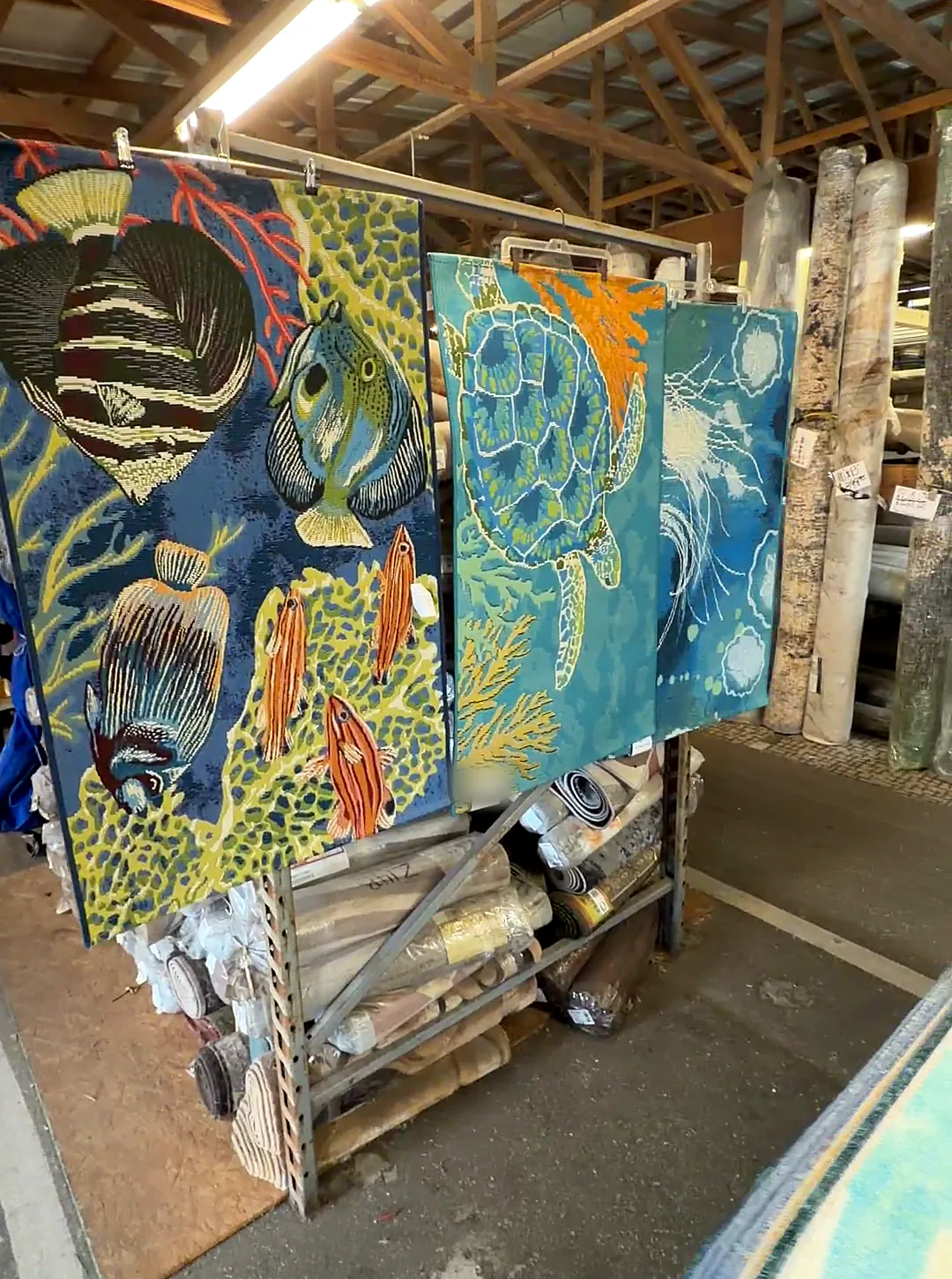 Bright sea-life rugs with angelfish and a sea turtle hanging on a rolling rack.