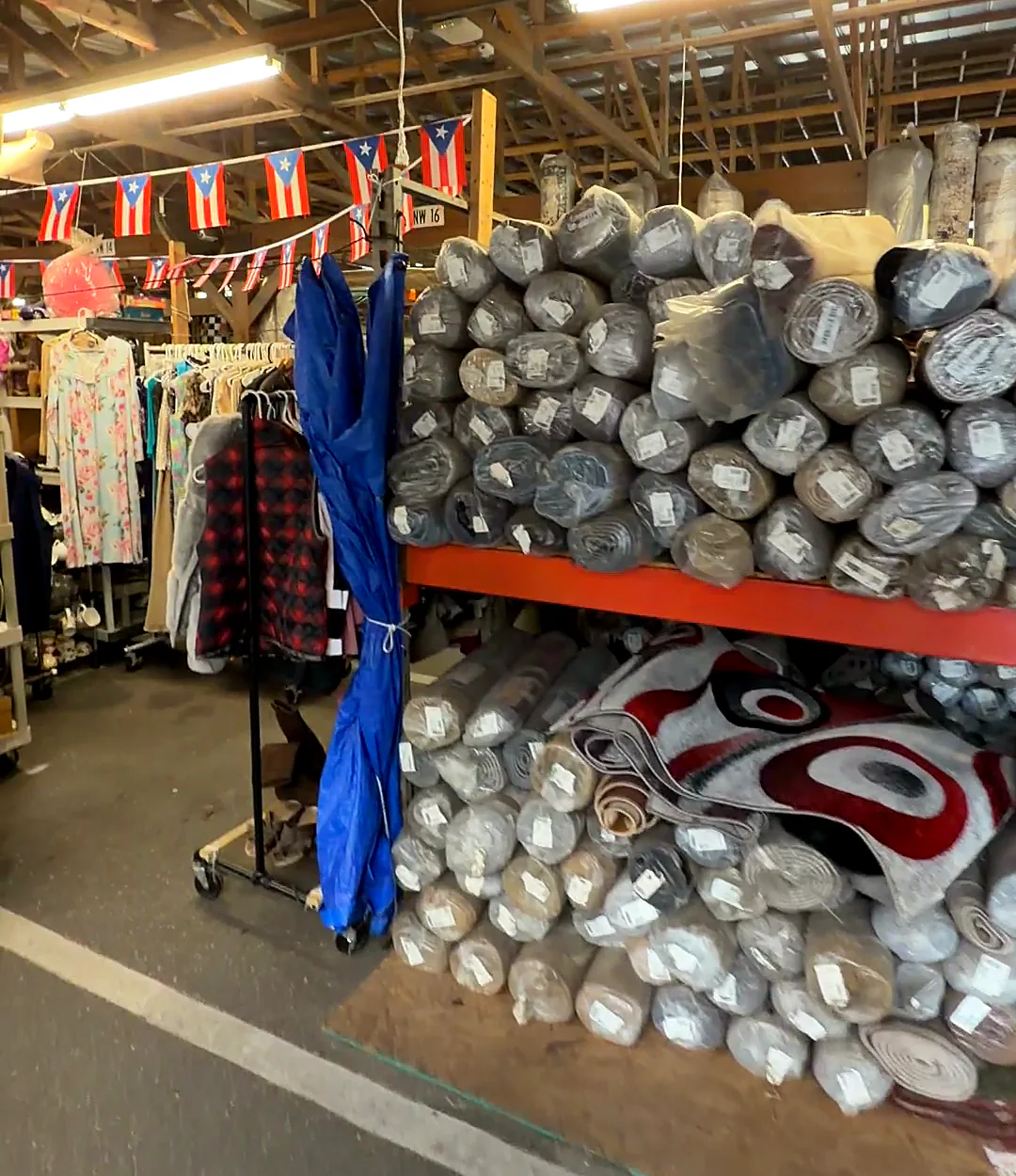 Red shelving stacked with plastic-wrapped rolled rugs, a red and white swirl rug in front.