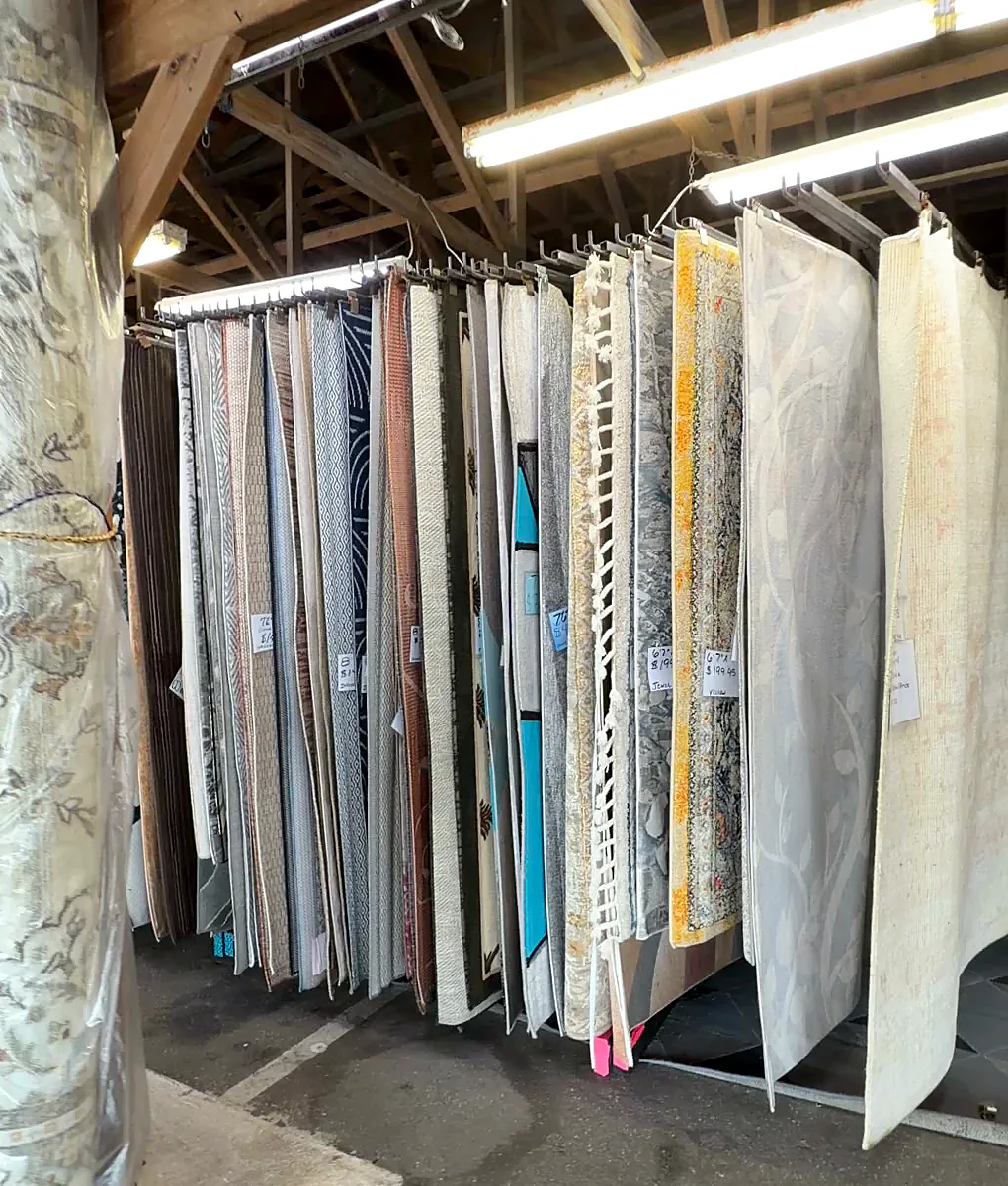 A long rack of rugs hanging side by side from the rafters.